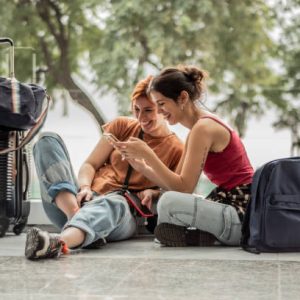 Young friends woman using phone sitting on ground while waiting at airport Young friends woman using phone sitting on ground while waiting at airport